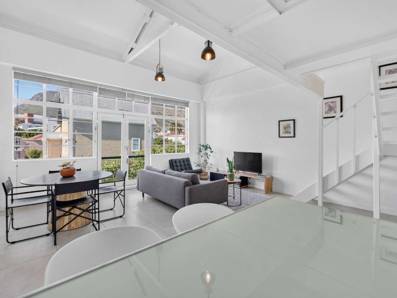 Bright open-plan living and dining area featuring vaulted ceilings with exposed rafters, large windows, and direct access to an outdoor space.