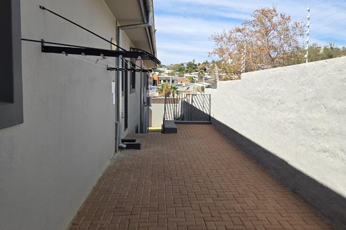 A paved side walkway featuring a boundary wall with electric fencing and a wall-mounted clothesline.