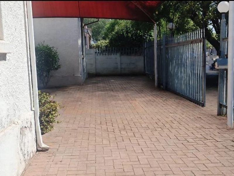 A paved driveway area featuring a metal security gate, perimeter walling, and a covered carport structure.