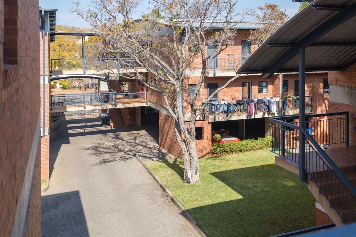 An elevated view of the apartment complex courtyard, featuring brick facade buildings, paved walkways, metal staircases, and a central garden area.
