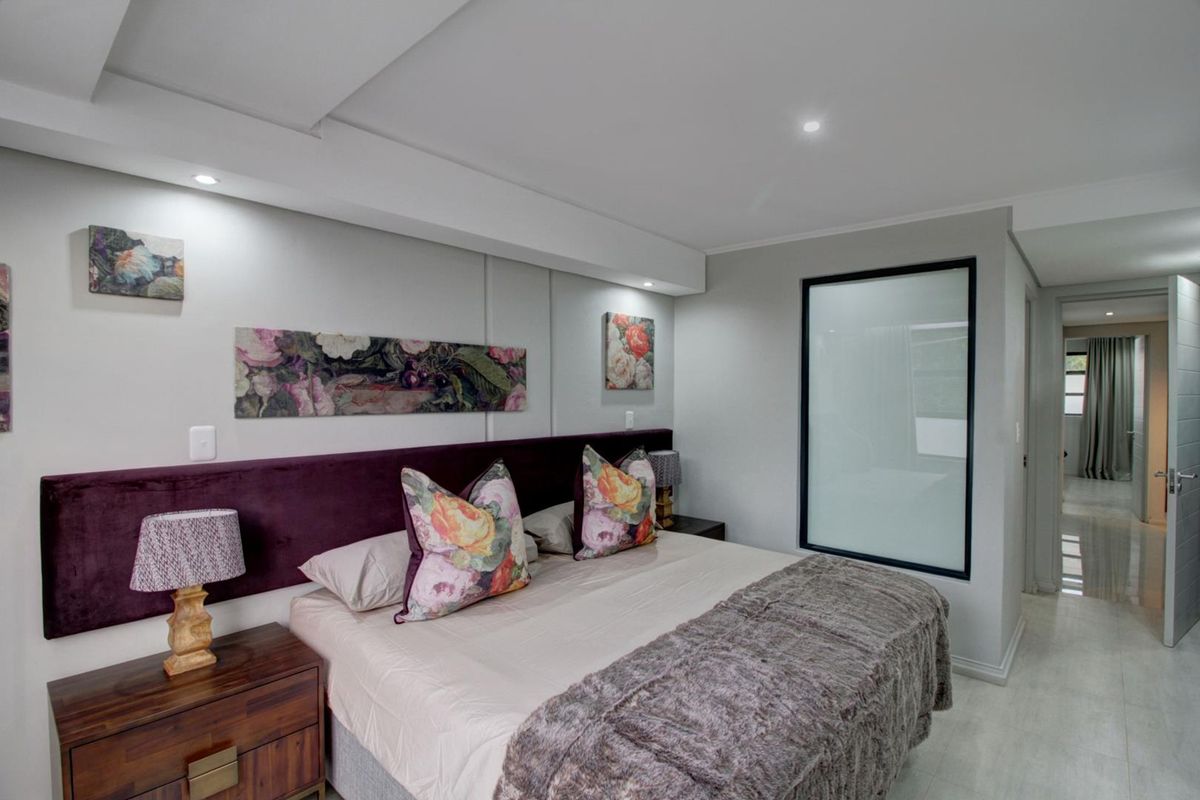 A well-maintained bedroom featuring a built-in headboard, recessed ceiling lighting, and a modern frosted glass partition providing a sleek, contemporary aesthetic.