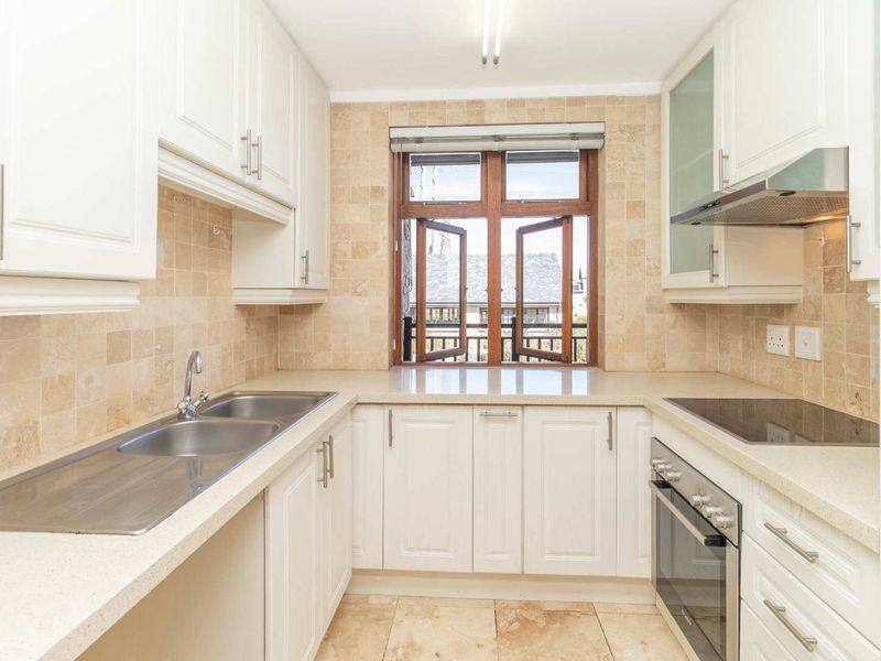 A clean, functional kitchen featuring white cabinetry, stone countertops, a double basin sink, and integrated appliances with a tiled backsplash and flooring.