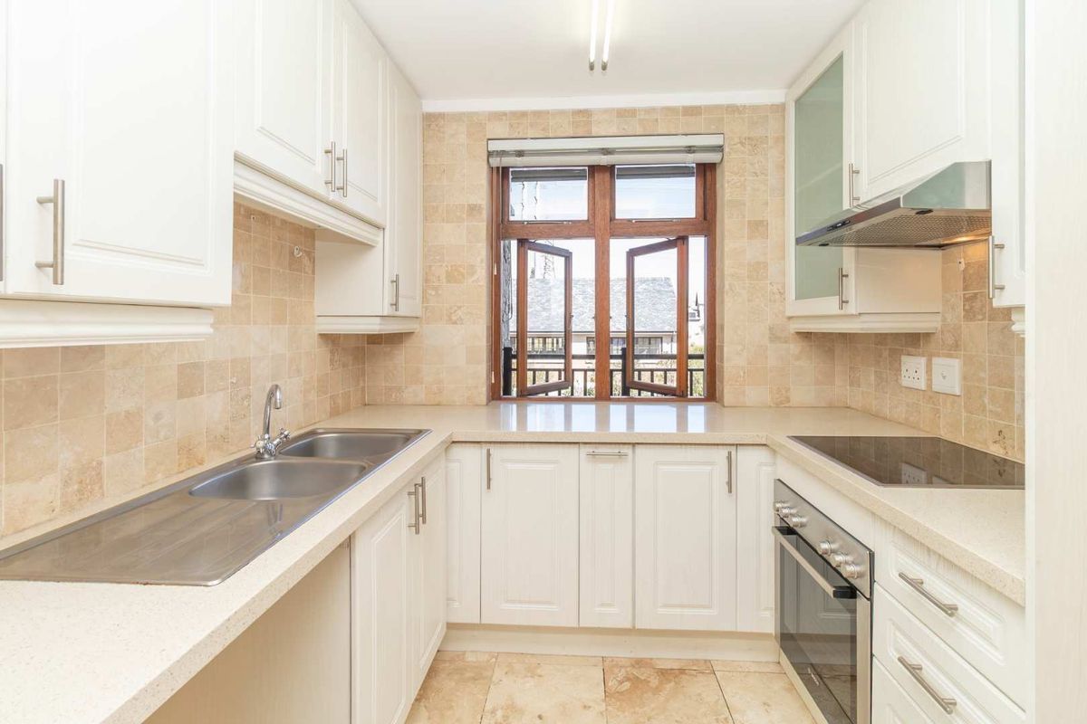 A clean, functional kitchen featuring white cabinetry, stone countertops, a double basin sink, and integrated appliances with a tiled backsplash and flooring.