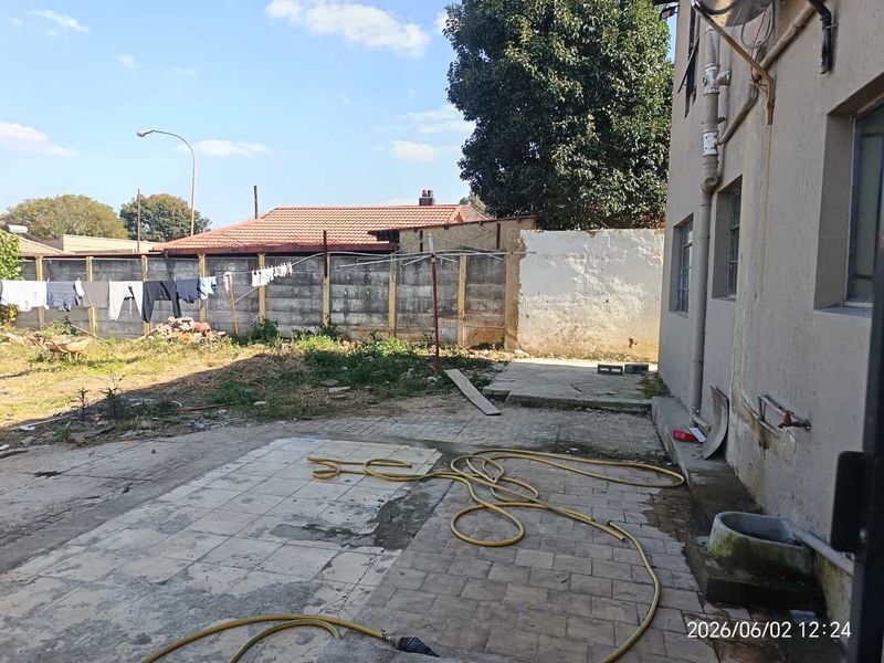 Rear exterior area featuring a paved patio, concrete boundary wall, and external water access, offering potential for landscaping and outdoor improvement.