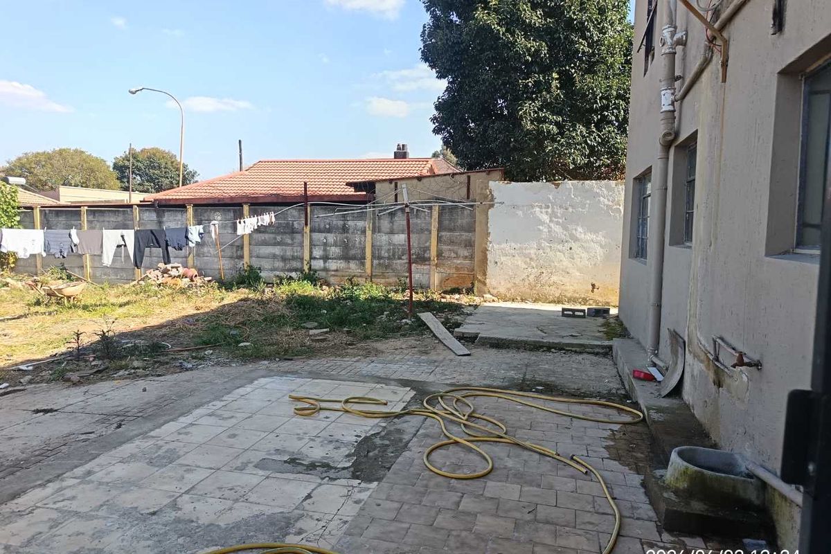 Rear exterior area featuring a paved patio, concrete boundary wall, and external water access, offering potential for landscaping and outdoor improvement.