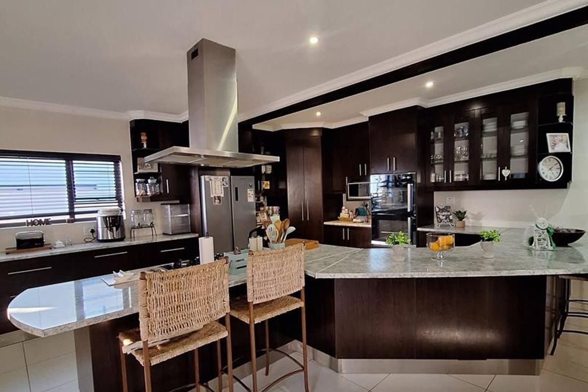 Spacious kitchen featuring dark wood cabinetry, granite countertops, a large central island with breakfast bar seating, and built-in stainless steel appliances.
