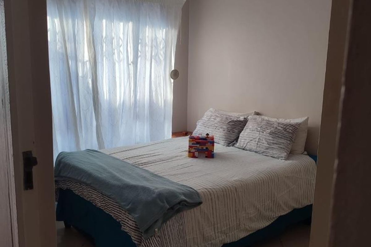 A standard bedroom featuring tiled flooring and large windows with curtains, providing a functional and well-lit living space.