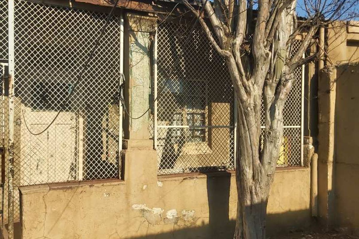 Rear exterior view of the property showing a masonry wall with security mesh fencing and signs of significant structural wear and weathering.