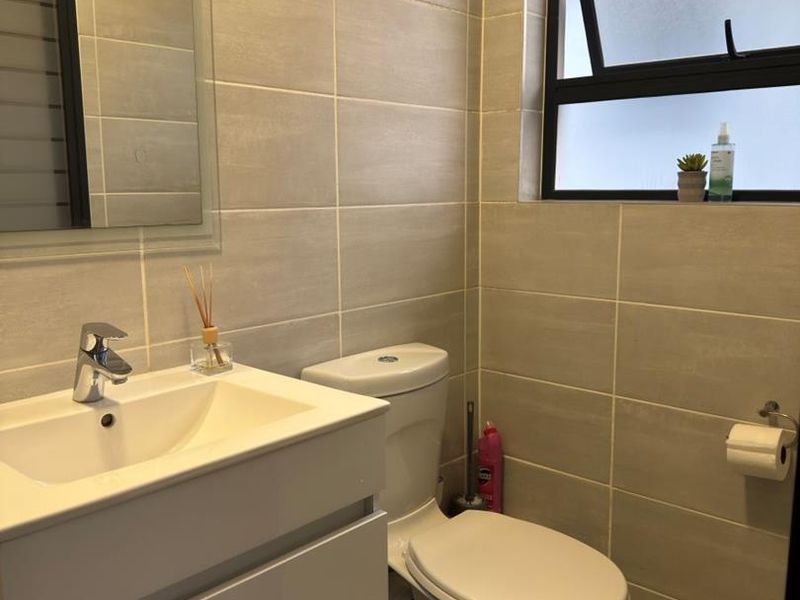 A modern, well-maintained bathroom featuring neutral wall tiles, a sleek vanity cabinet with a basin, and a functional top-hung window for ventilation.