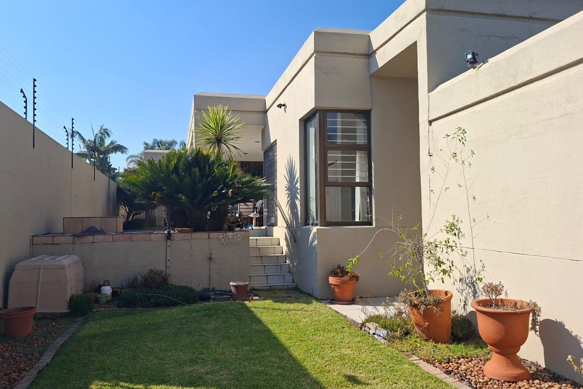 Rear exterior view of the townhouse featuring a private garden, boundary walls with electric fencing, and access steps to the main living area.