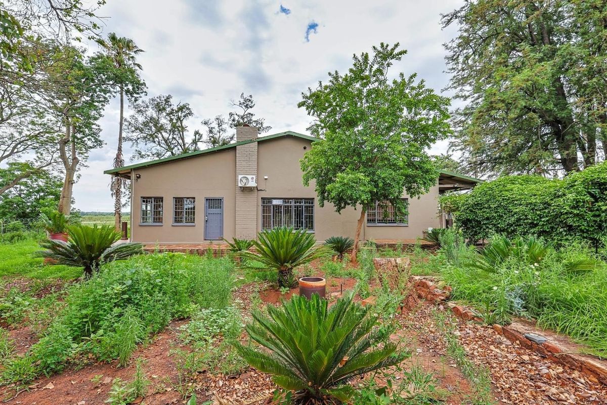 Rear view of the commercial property featuring a brick facade, security bars on windows, and an established garden with mature trees and shrubs.
