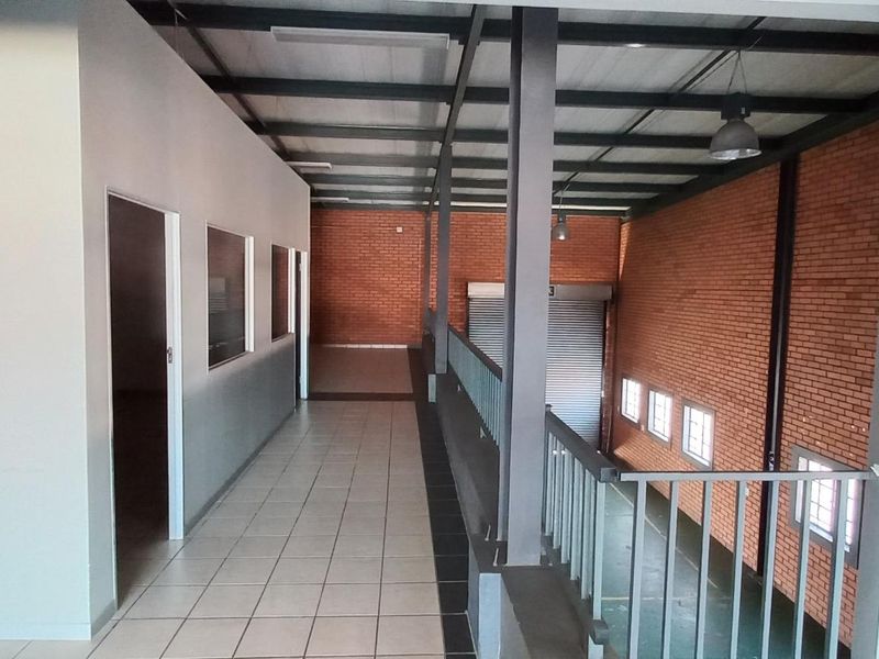 An industrial mezzanine level featuring exposed brick walls, tiled flooring, steel structural beams, and a metal railing overlooking the lower warehouse area.