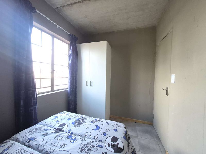 A bedroom featuring tiled flooring, a built-in wardrobe, and an exposed concrete ceiling, offering a functional space with potential for cosmetic updates.
