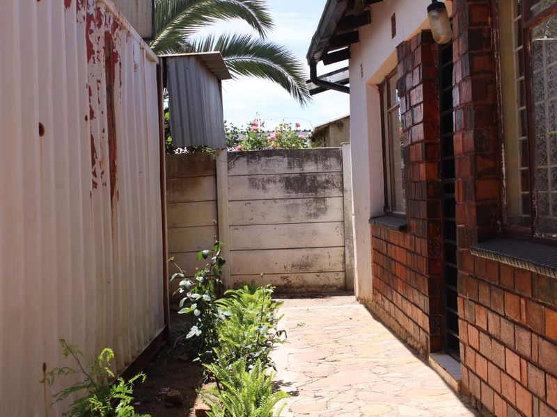 A narrow side passage featuring a paved walkway, brick exterior wall with security bars, and a weathered metal structure.