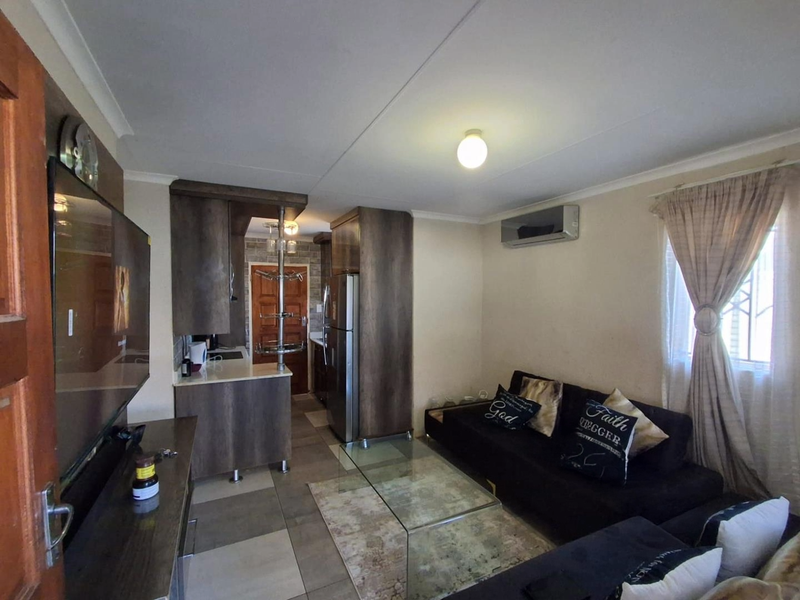 Open-plan living area featuring a compact kitchen with built-in cabinetry, stone countertops, and a wall-mounted air conditioning unit.
