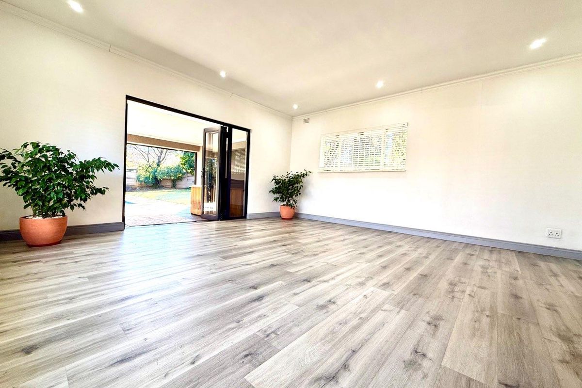 Bright and spacious living area featuring modern wood-look laminate flooring, recessed downlighting, and large glass sliding doors opening to the outdoor patio.