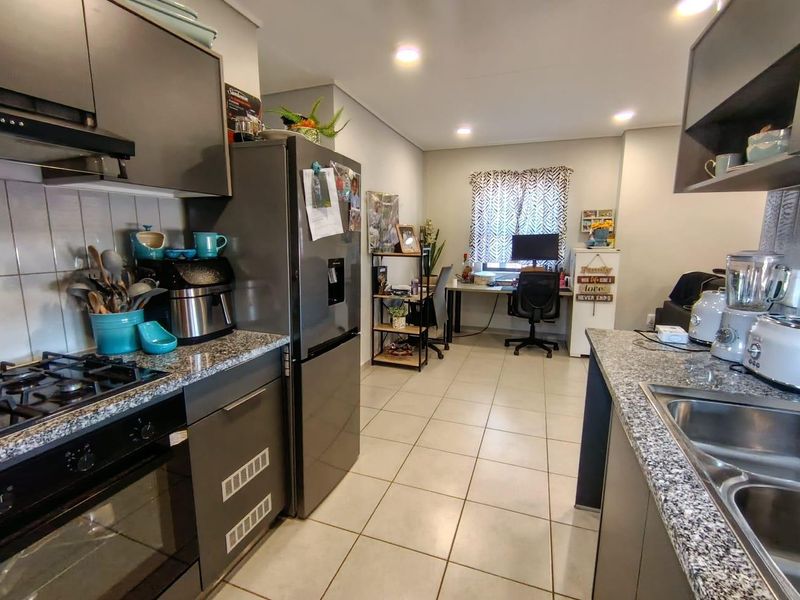 Open-plan kitchen featuring modern grey cabinetry, granite countertops, and integrated appliances, flowing into a functional workspace area with tiled flooring throughout.