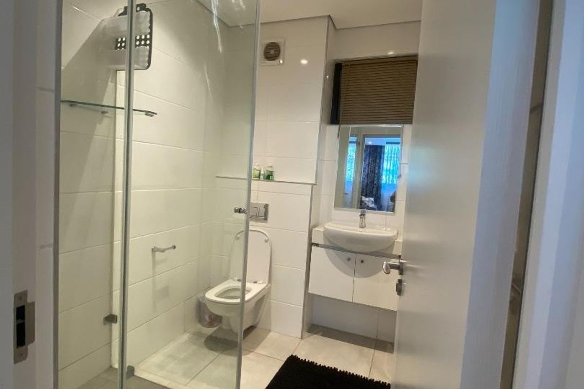 Modern bathroom featuring a glass-enclosed shower, wall-mounted toilet, and a vanity unit with a basin, finished with neutral floor tiles.