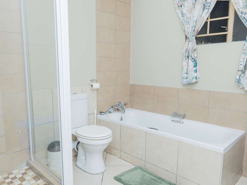 A functional bathroom featuring a bathtub, separate shower enclosure, and toilet with neutral wall and floor tiling.