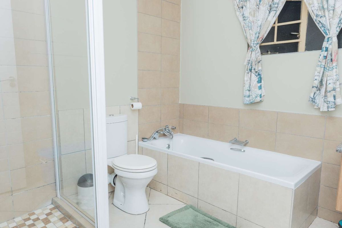 A functional bathroom featuring a bathtub, separate shower enclosure, and toilet with neutral wall and floor tiling.