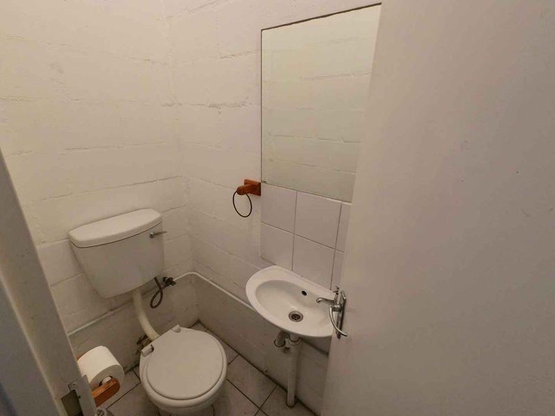 A compact industrial-style restroom featuring a basic toilet, wall-mounted basin, and exposed blockwork walls.