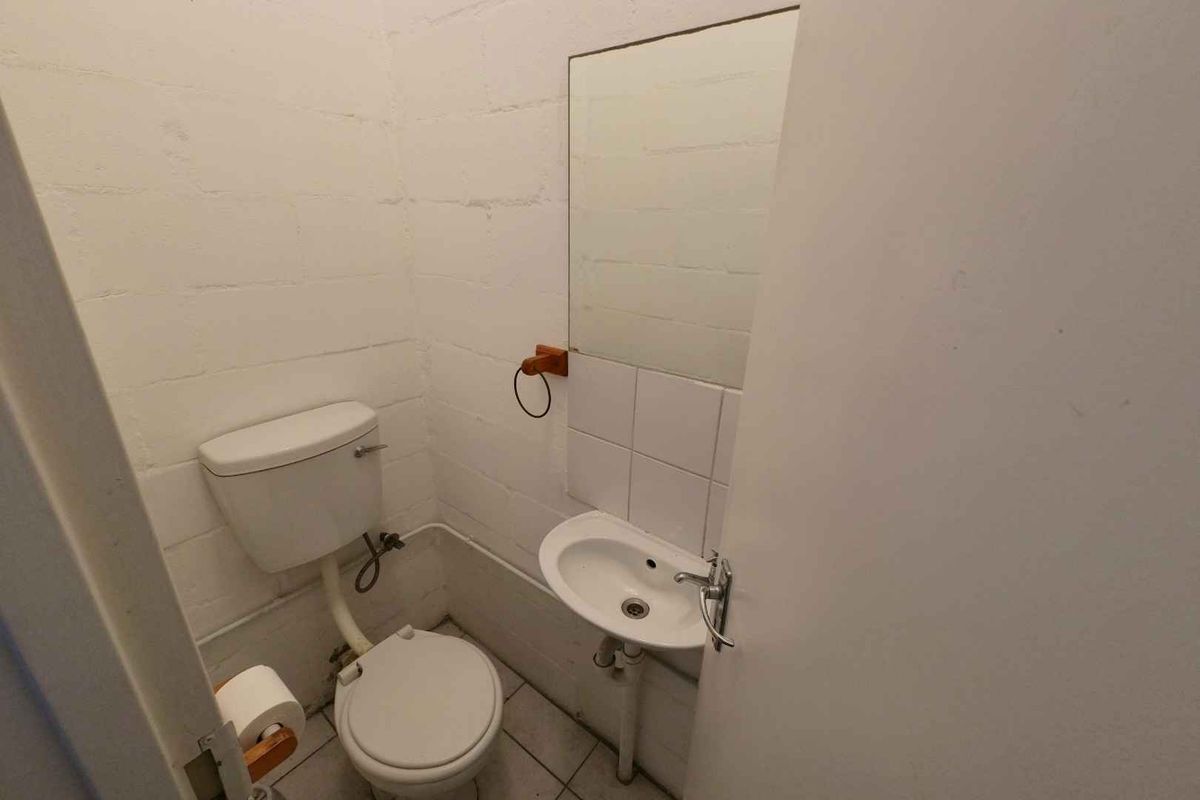 A compact industrial-style restroom featuring a basic toilet, wall-mounted basin, and exposed blockwork walls.