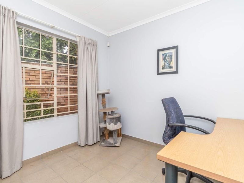 A functional office space featuring tiled flooring, neutral walls, and a window fitted with security bars.
