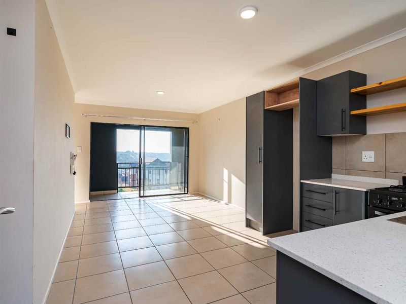 Modern open-plan living area featuring a sleek kitchen with dark cabinetry, stone countertops, tiled floors, and direct access to a private balcony.
