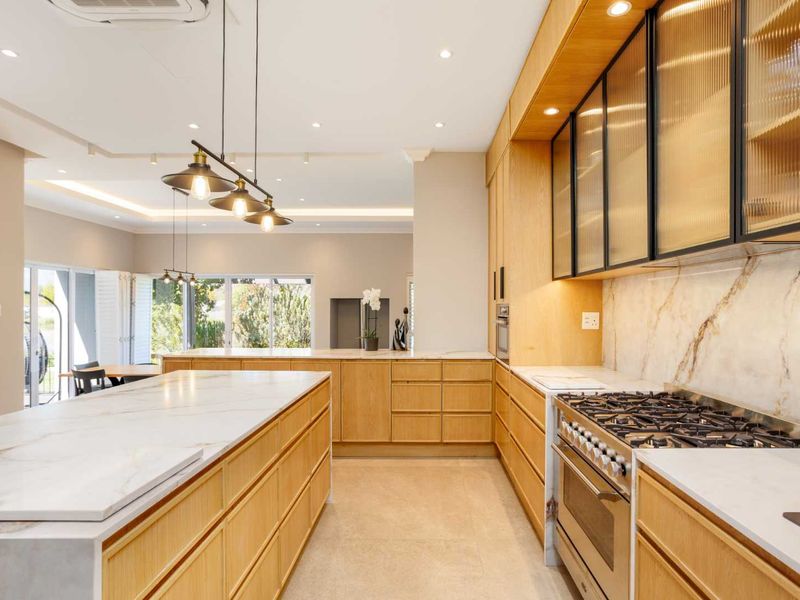 Modern open-plan kitchen featuring high-end wooden cabinetry, marble countertops, a large central island, and premium integrated appliances with elegant fluted glass accents.