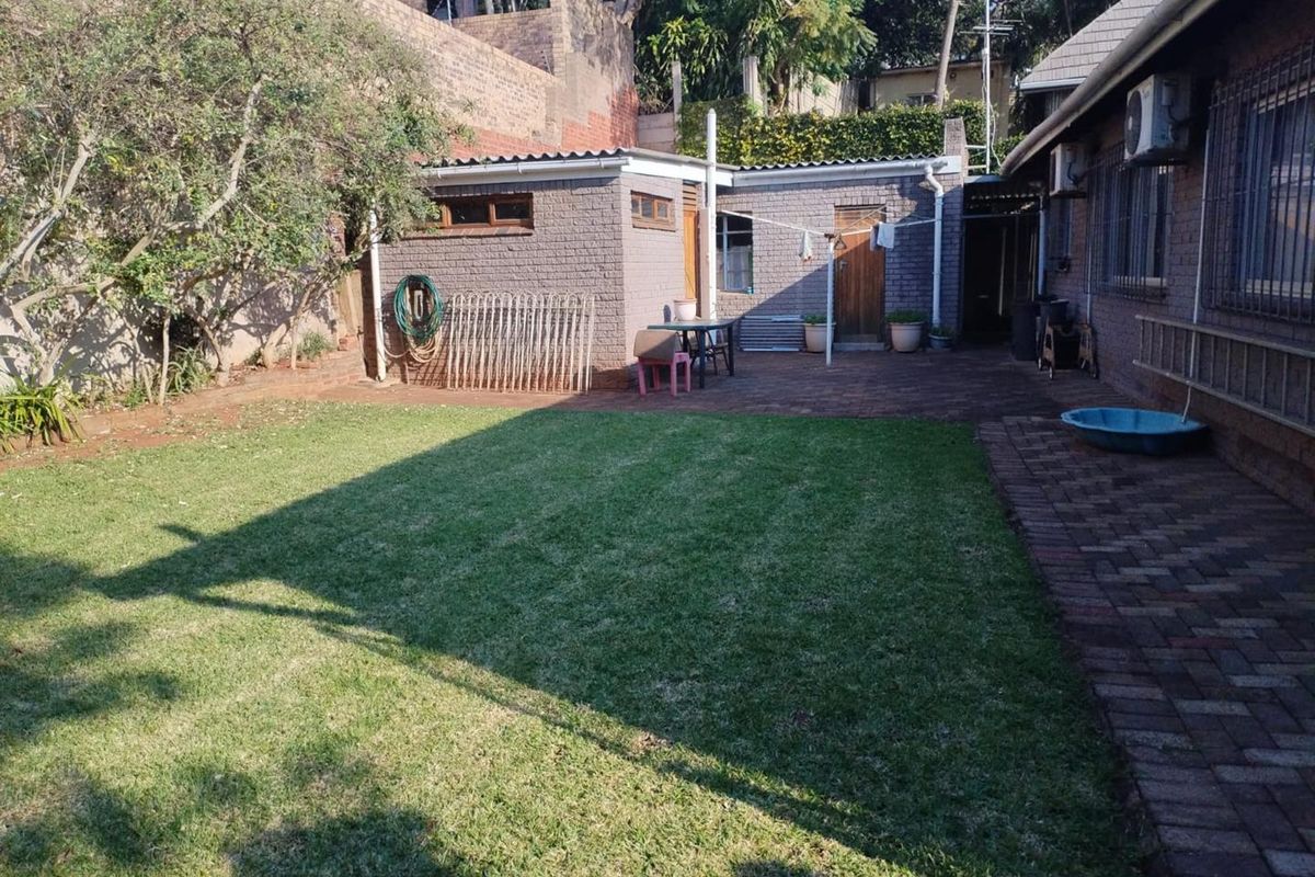 A rear garden area featuring a brick-paved patio, a well-maintained lawn, and a brick outbuilding with security features.