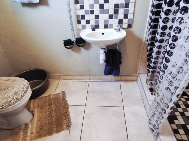 A compact bathroom featuring a wall-mounted basin, toilet, and shower area with mosaic tile accents and neutral floor tiling.