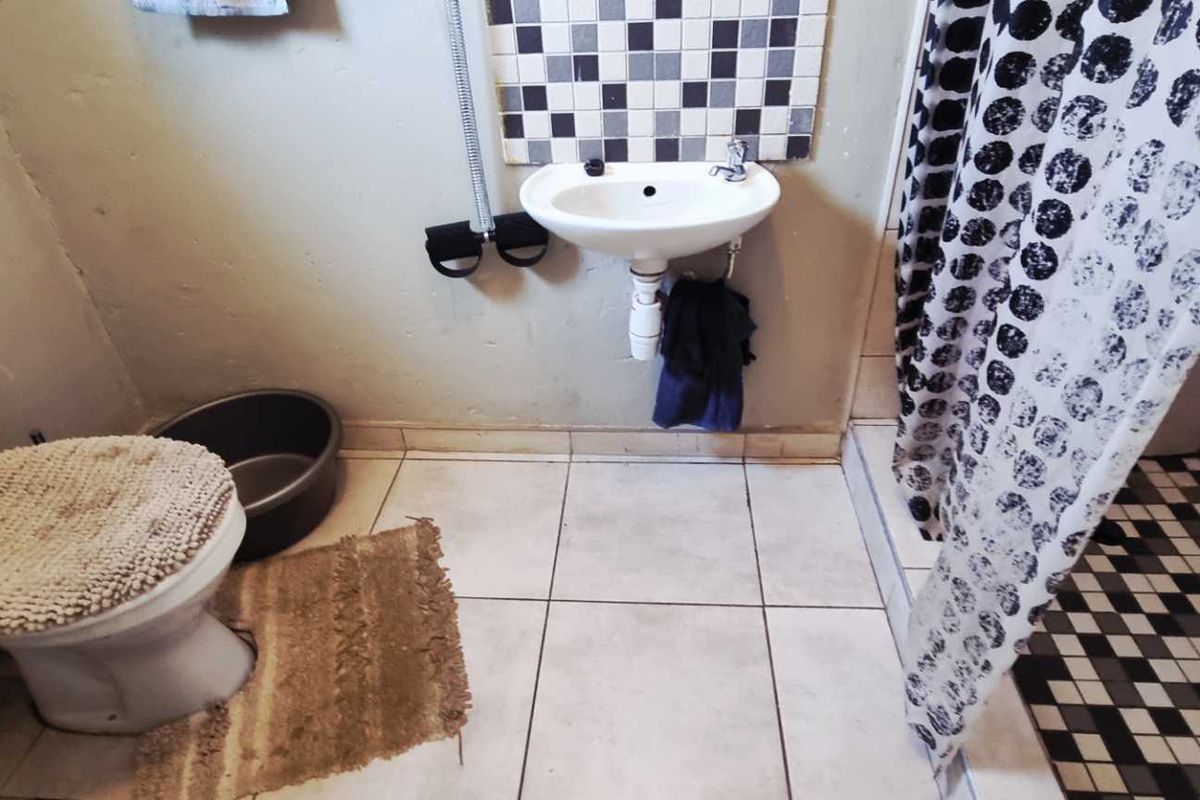 A compact bathroom featuring a wall-mounted basin, toilet, and shower area with mosaic tile accents and neutral floor tiling.