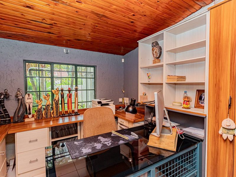 A functional home office featuring built-in cabinetry, a desk workspace, and a timber-clad ceiling with a window overlooking the garden.