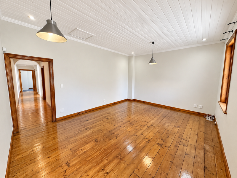 An empty living room featuring polished timber flooring, a white tongue and groove ceiling, and classic timber door and window frames.
