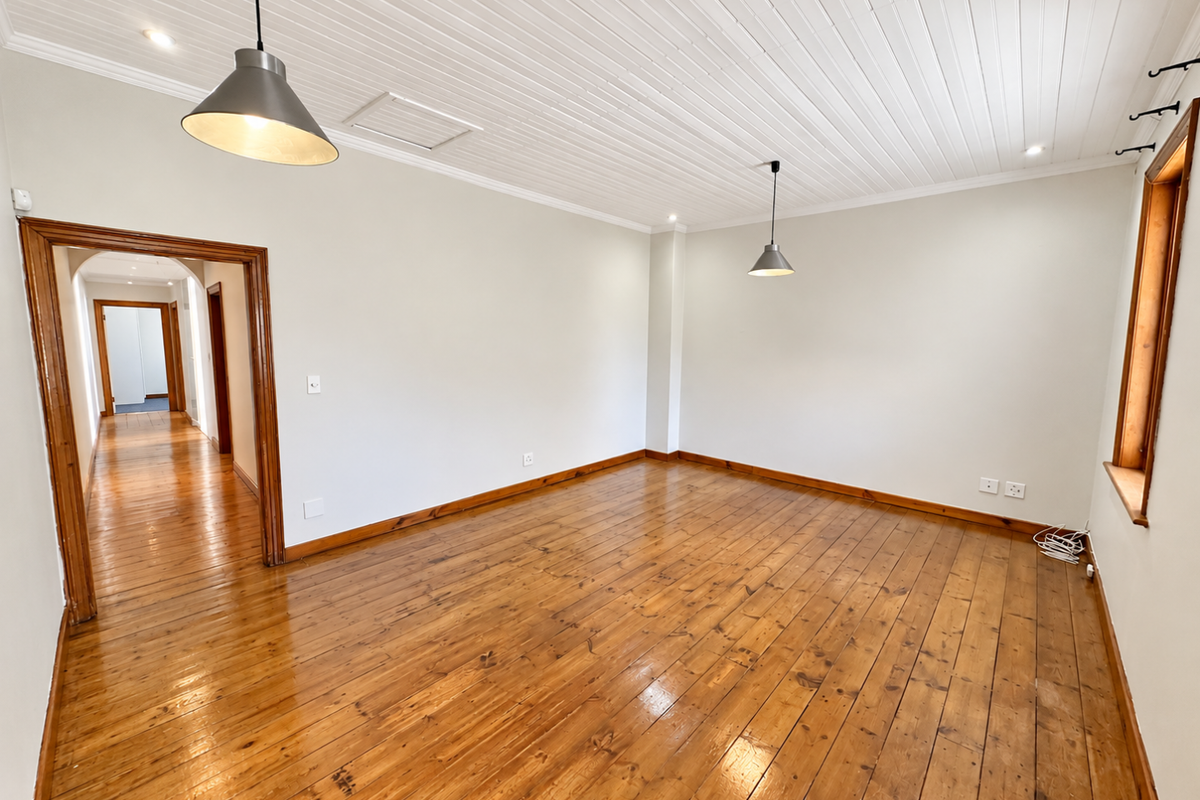 An empty living room featuring polished timber flooring, a white tongue and groove ceiling, and classic timber door and window frames.