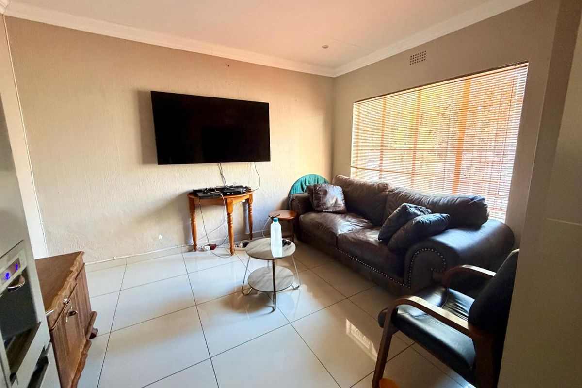 A functional living room featuring large format floor tiles, recessed ceiling lighting, and a window fitted with wooden venetian blinds.