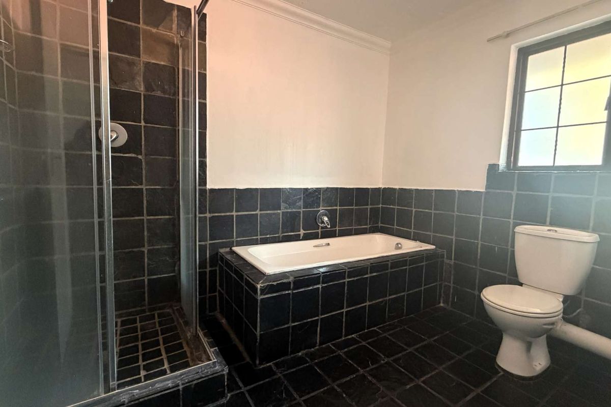 A dated bathroom featuring a built-in bathtub, separate shower enclosure, and toilet, finished with dark tiled flooring and wall cladding.