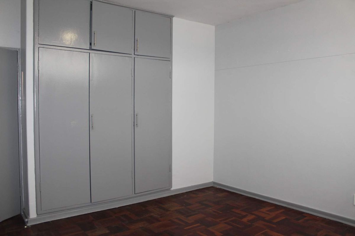 A clean, empty bedroom featuring classic parquet flooring and ample built-in cupboard storage with a neutral grey and white color scheme.