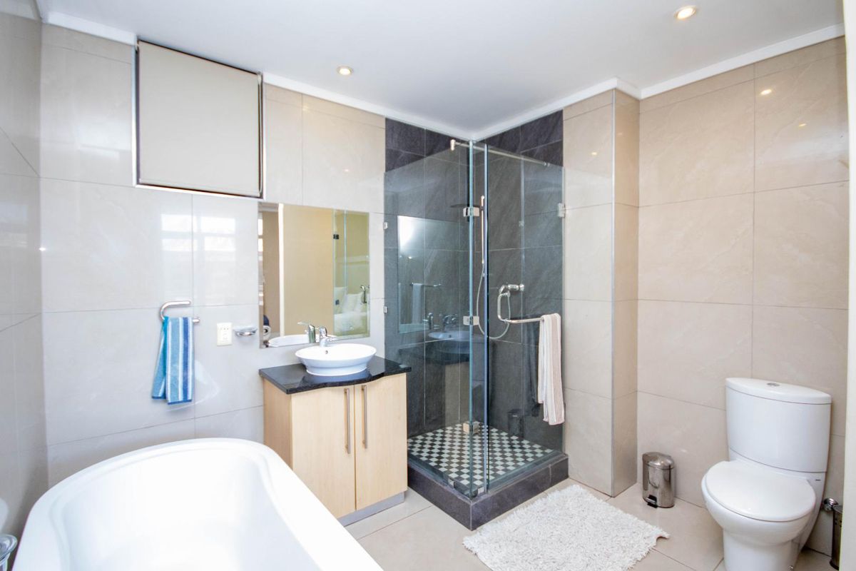 Modern bathroom featuring a glass-enclosed shower, vessel sink vanity, bathtub, and neutral wall tiling with contemporary fixtures.