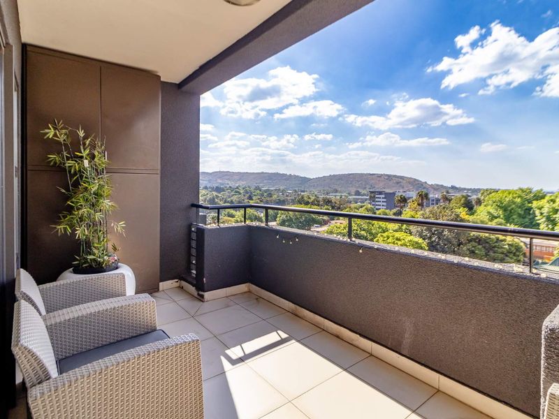 A spacious covered balcony featuring tiled flooring, a secure metal balustrade, and a built-in storage cupboard, offering expansive elevated views.