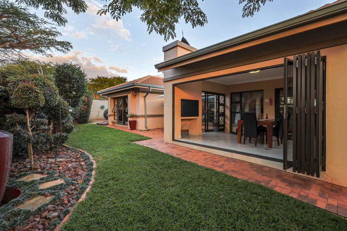 A well-maintained rear garden featuring a manicured lawn, brick pathways, and a covered patio with large folding doors leading into the home.
