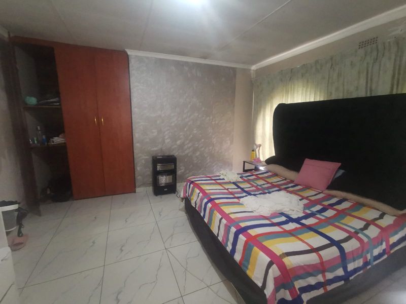 A bedroom featuring tiled flooring, a built-in wardrobe, and a textured feature wall, offering a functional space with potential for cosmetic updates.
