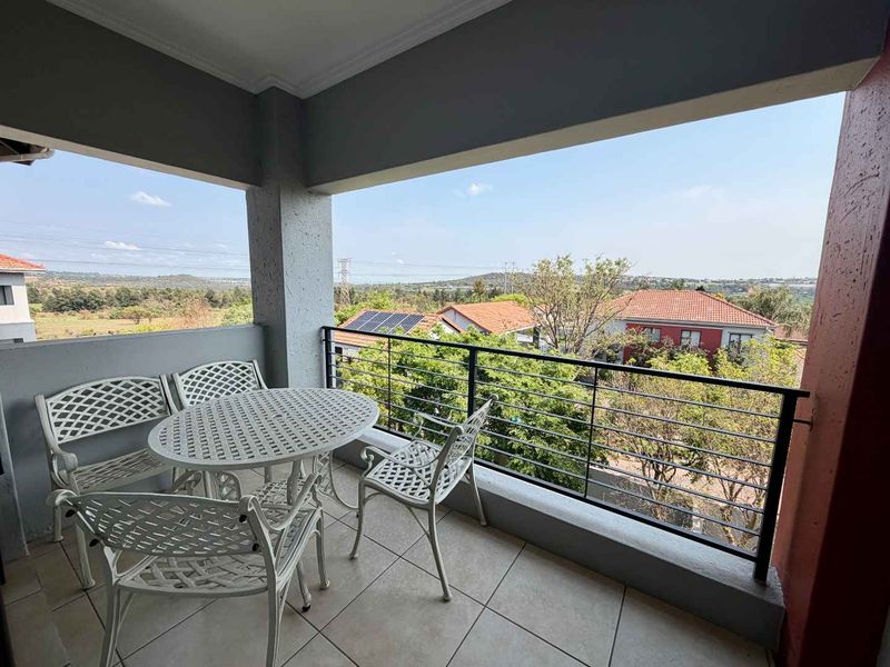 A covered balcony featuring tiled flooring and a metal railing, offering an elevated view of the surrounding neighborhood and landscape.