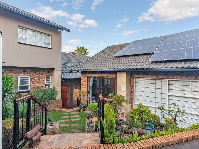 A well-maintained rear exterior view featuring a brick and stone facade, tiled roof with solar panels, and a landscaped garden with paved steps.
