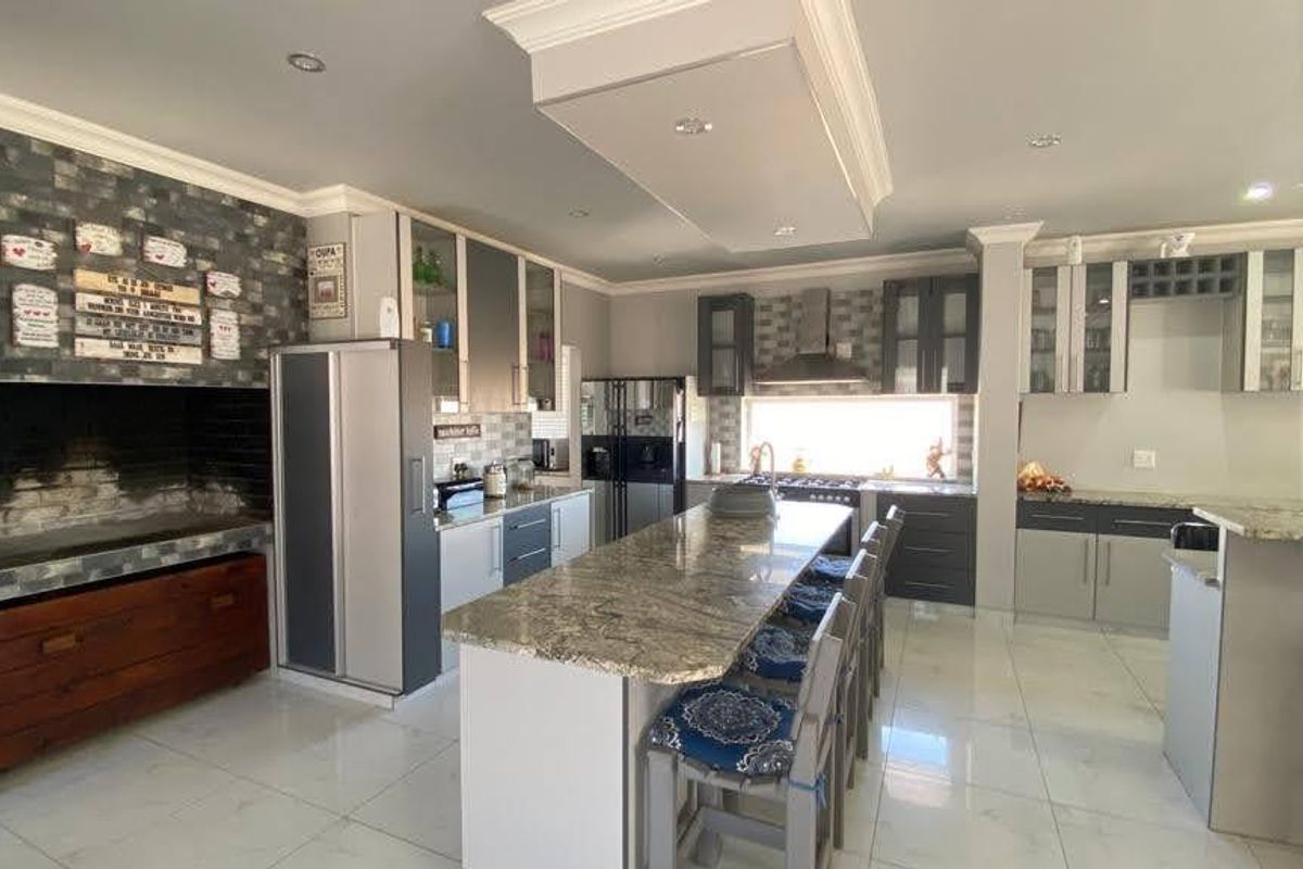 Spacious modern kitchen featuring a large granite-topped island, extensive built-in cabinetry, and a unique integrated indoor braai area with stone cladding.