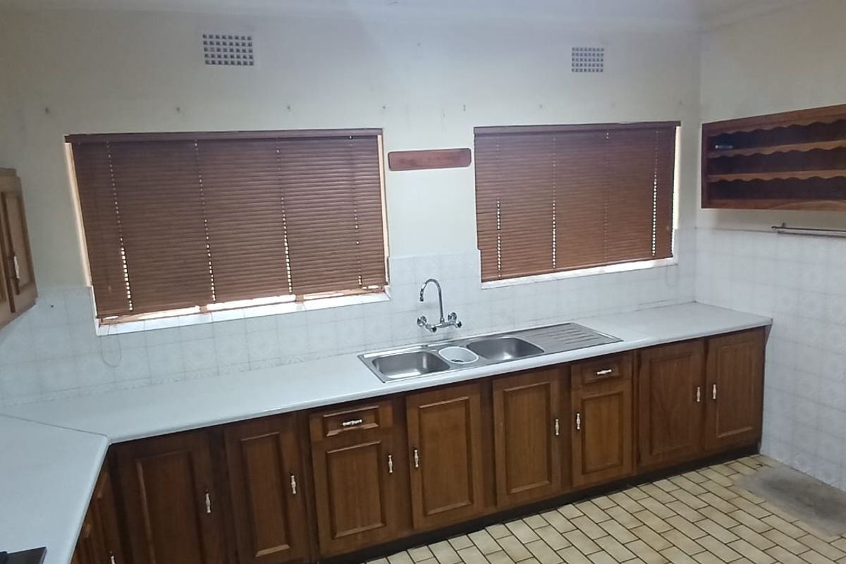 A functional kitchen featuring wooden cabinetry, a double-basin sink, tiled splashbacks, and tiled flooring, offering a classic layout with ample counter space.