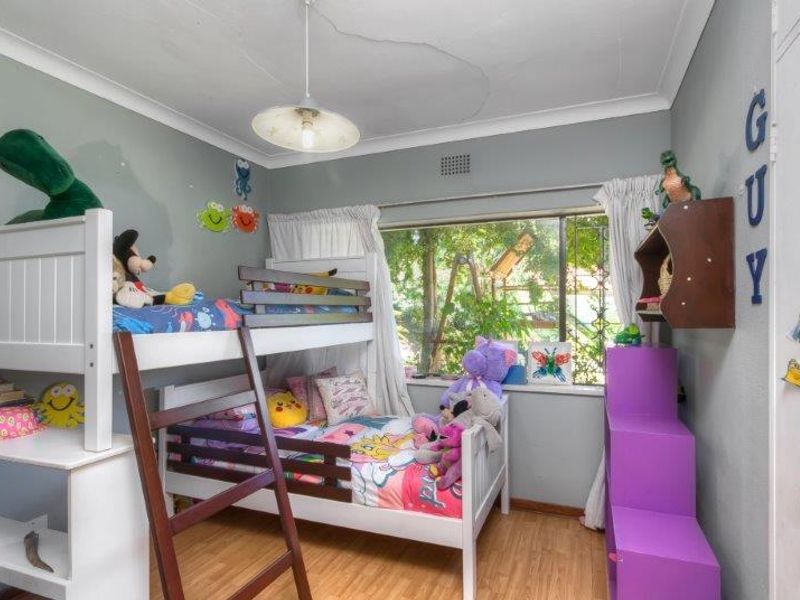 A bedroom featuring laminate flooring, a ceiling light fixture, and security bars on the window. The ceiling shows visible signs of cracking.