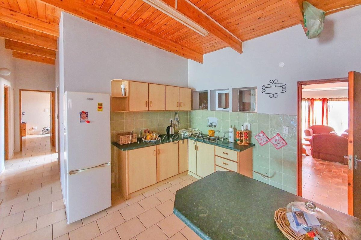A functional kitchen featuring light wood cabinetry, green tiled splashbacks, and a breakfast bar, set under a vaulted timber-beamed ceiling.