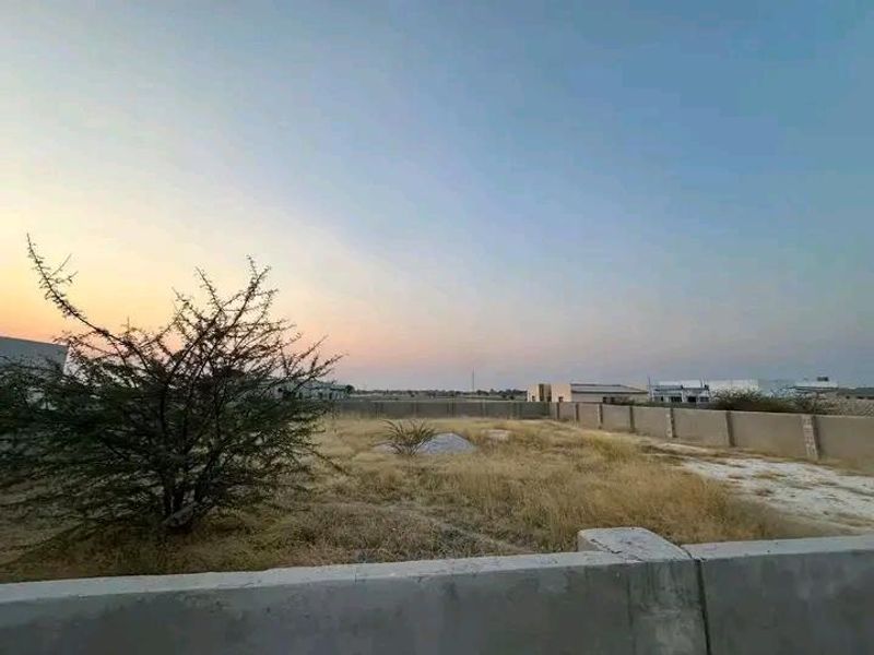 A view of a vacant commercial plot featuring a perimeter boundary wall and natural ground cover.