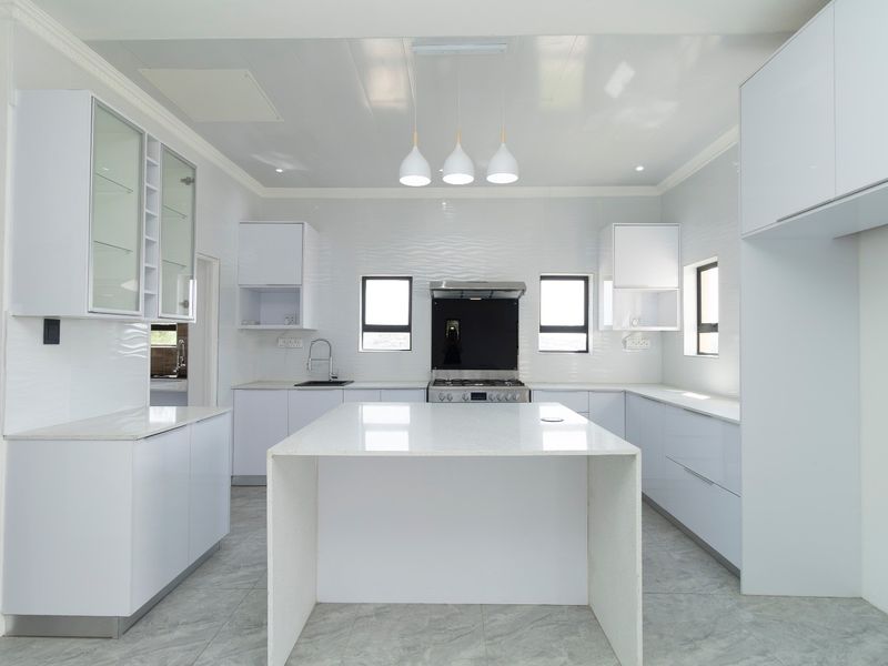 A modern, bright kitchen featuring white gloss cabinetry, a central island with quartz countertops, integrated appliances, and sleek tiled flooring.
